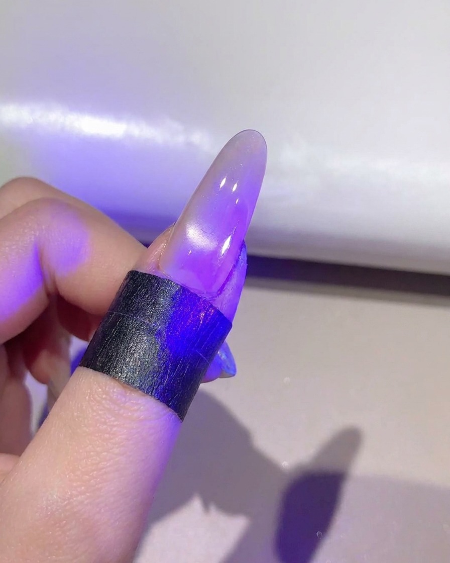 Paznokieć pod fioletową lampą UV/LED utwardzający ukończoną warstwę żelu cat-eye.