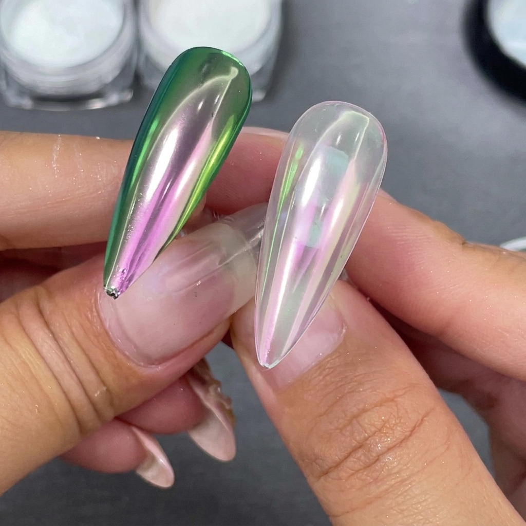 Dwa gotowe paznokcie stiletto trzymane obok siebie, jeden z jasną bazą, a drugi z czarną bazą pokazującą zielono-fioletowy refleks.