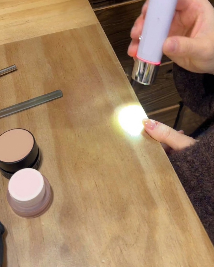 Przenośna lampa UV/LED utwardzająca ostateczną błyszczącą warstwę nawierzchniową na wypielęgnowanej dłoni.