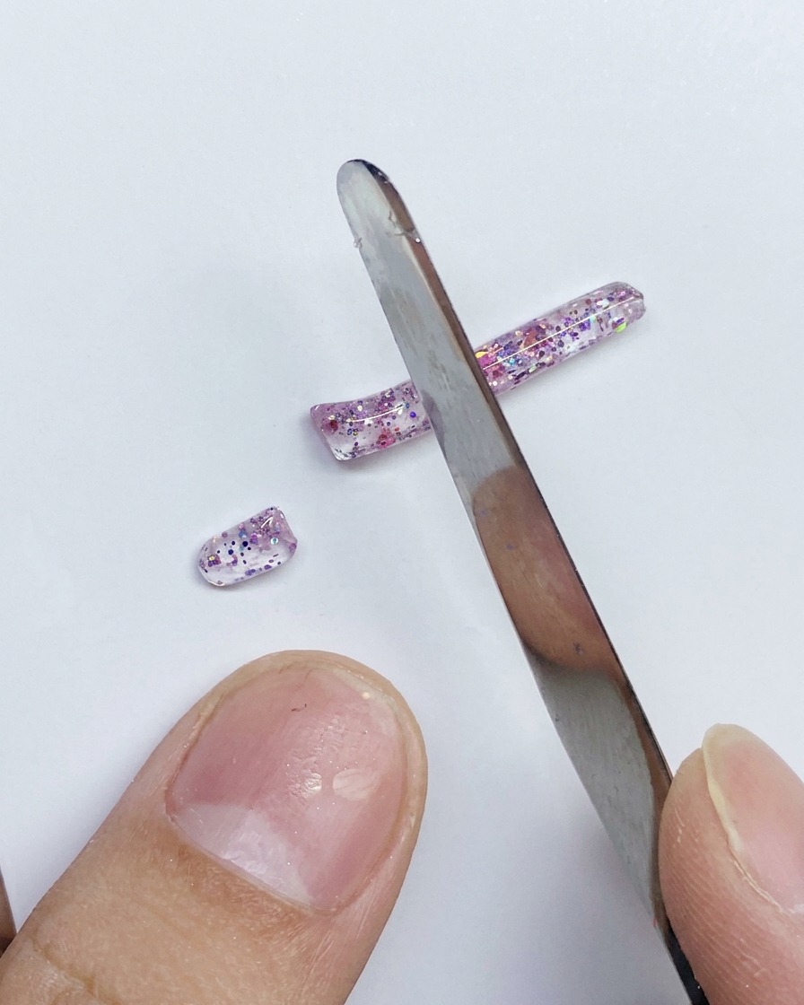 Metalowa szpatułka dzieląca długi pasek brokatowego, różowego żelu PVC na mniejsze segmenty.