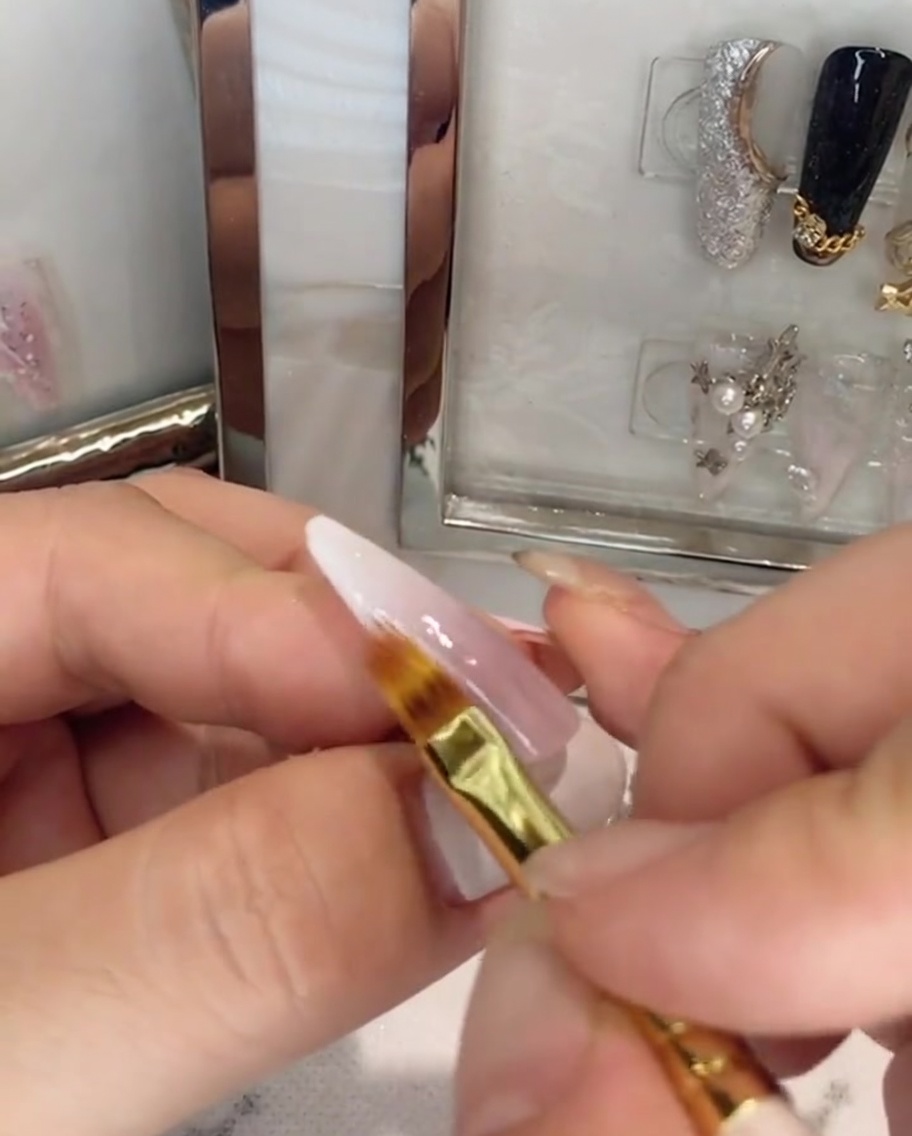 Pędzelek nakładający bezbarwny top coat na różowo-biały paznokieć ombre.