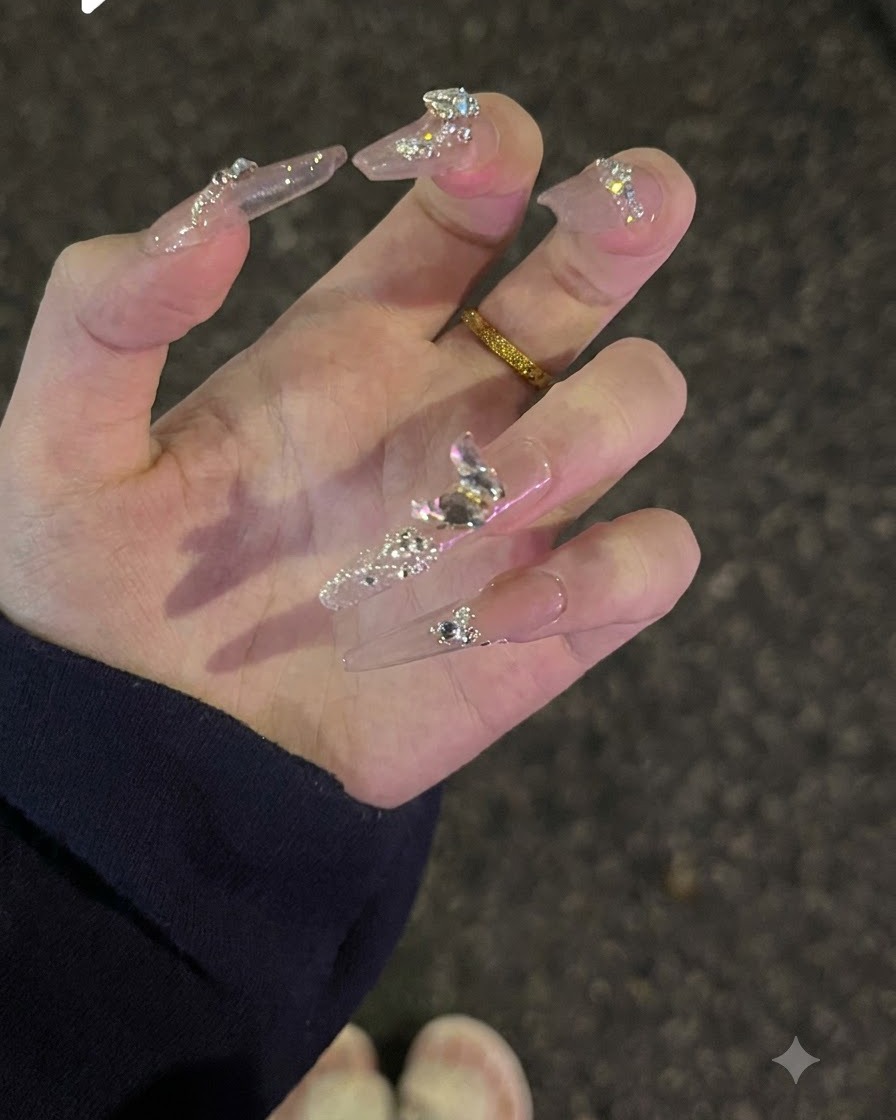 Dłoń odwrócona do góry, ukazująca brokat na powierzchni oraz lśniące kryształki diamentowe na paznokciach nude.