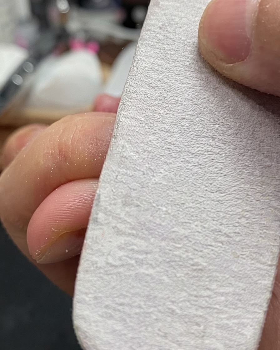 Eine Hand hält einen weißen Nagelbuffer und feilt leicht die Oberfläche eines natürlichen Fingernagels.