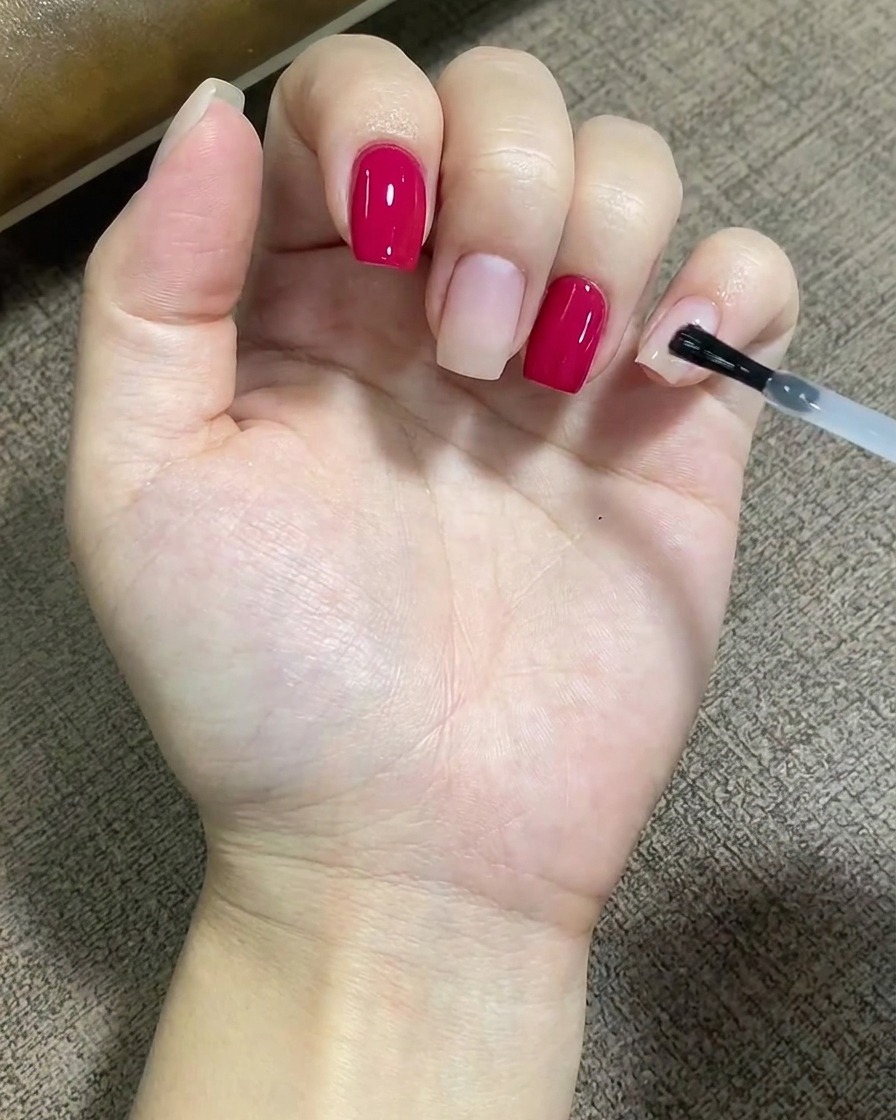 Ein Pinsel trägt eine klare Schicht Base Coat gleichmäßig auf die Oberfläche eines Fingernagels auf.