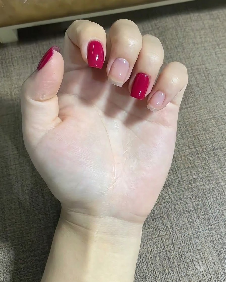Eine Nahaufnahme einer Hand mit einem feinen Liner-Pinsel zum Auftragen kleiner roter Punkte in der Nähe eines Sterndesigns auf dem Mittelfingernagel.