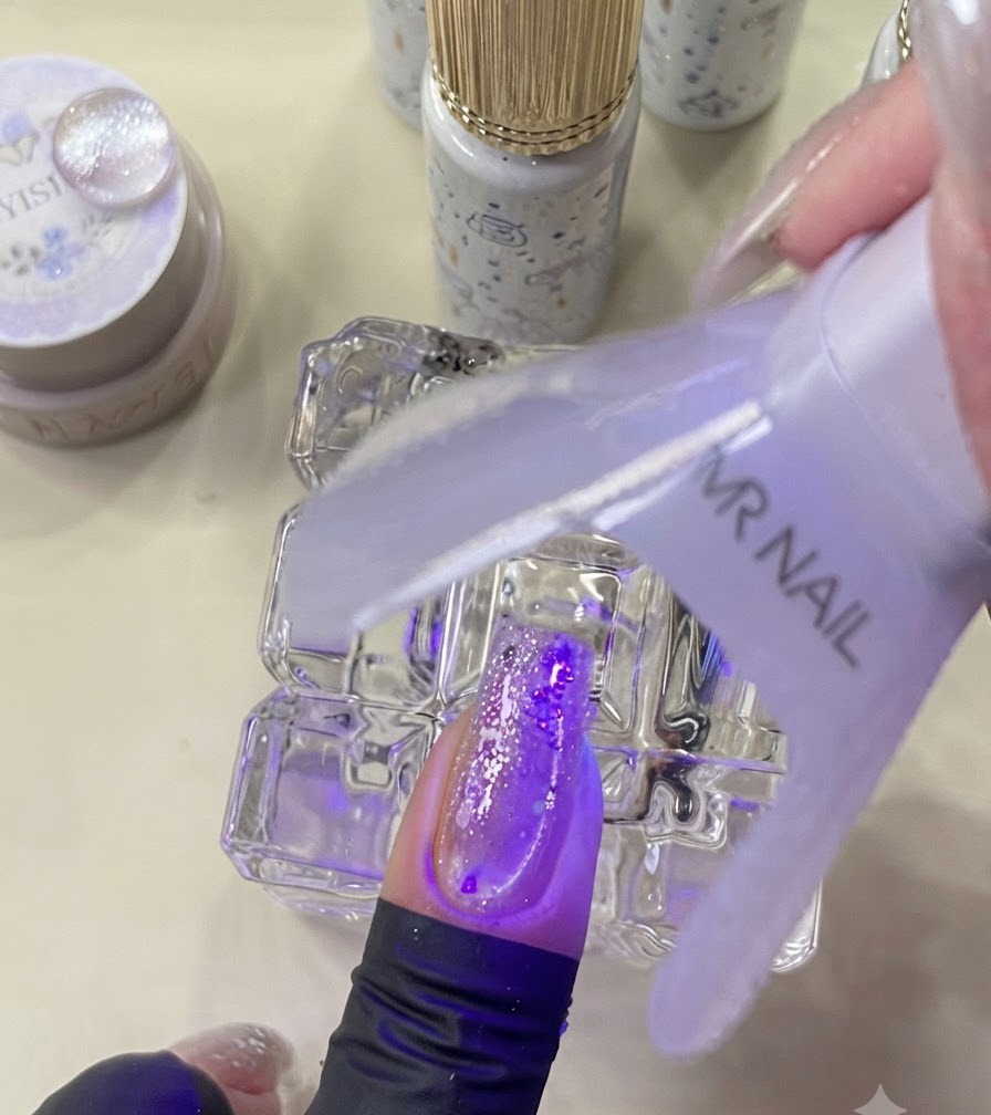 Mini lampa UV utwardzająca ozdobiony paznokieć pod fioletowym światłem.