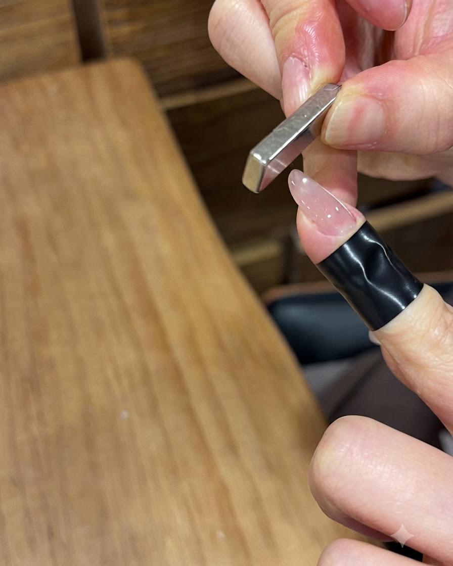Ein rechteckiger Stabmagnet wird vertikal in die Nähe eines lackierten Nagels gehalten.