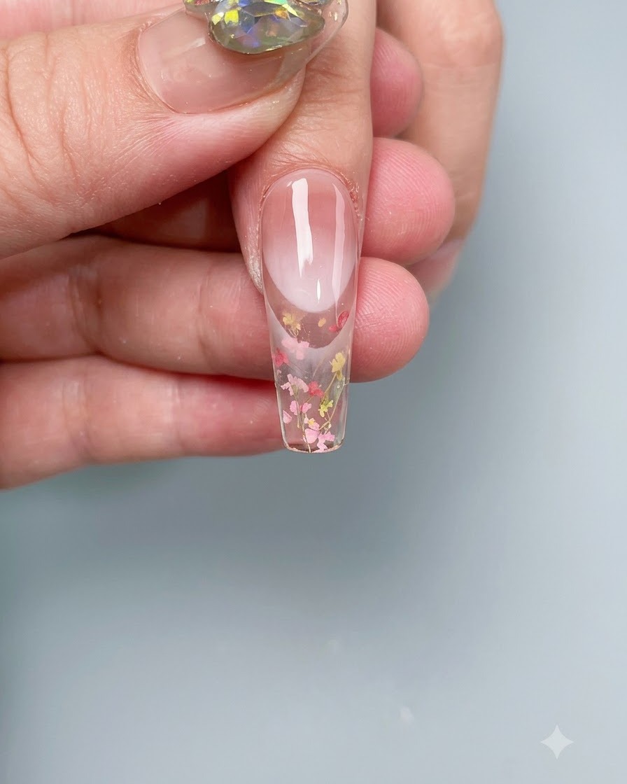 Paznokieć z zatopionymi suszonymi kwiatami utwardzający się w profesjonalnej lampie UV/LED.