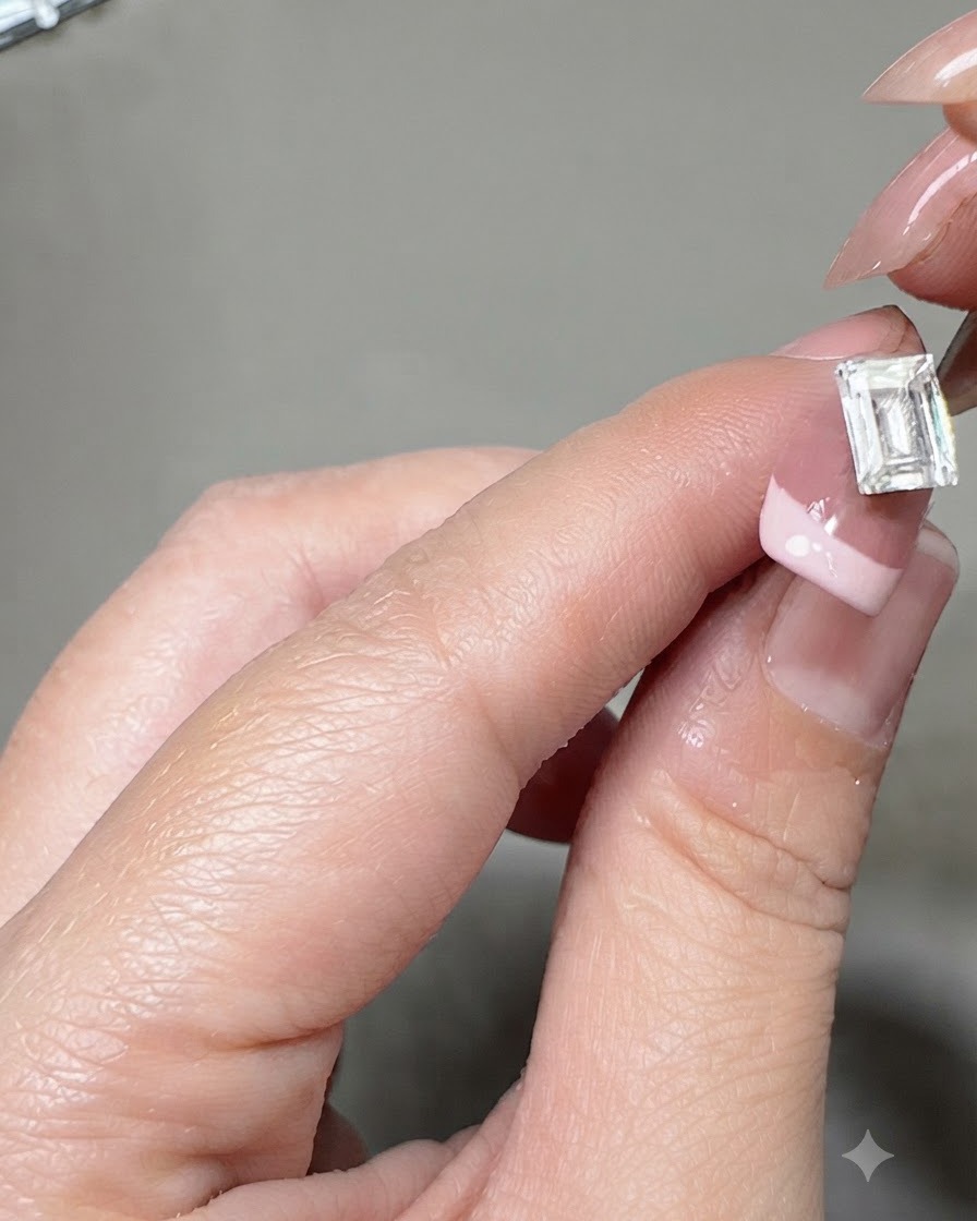 Pęseta umieszczająca duży prostokątny kryształ na środku paznokcia z francuskim manicure.