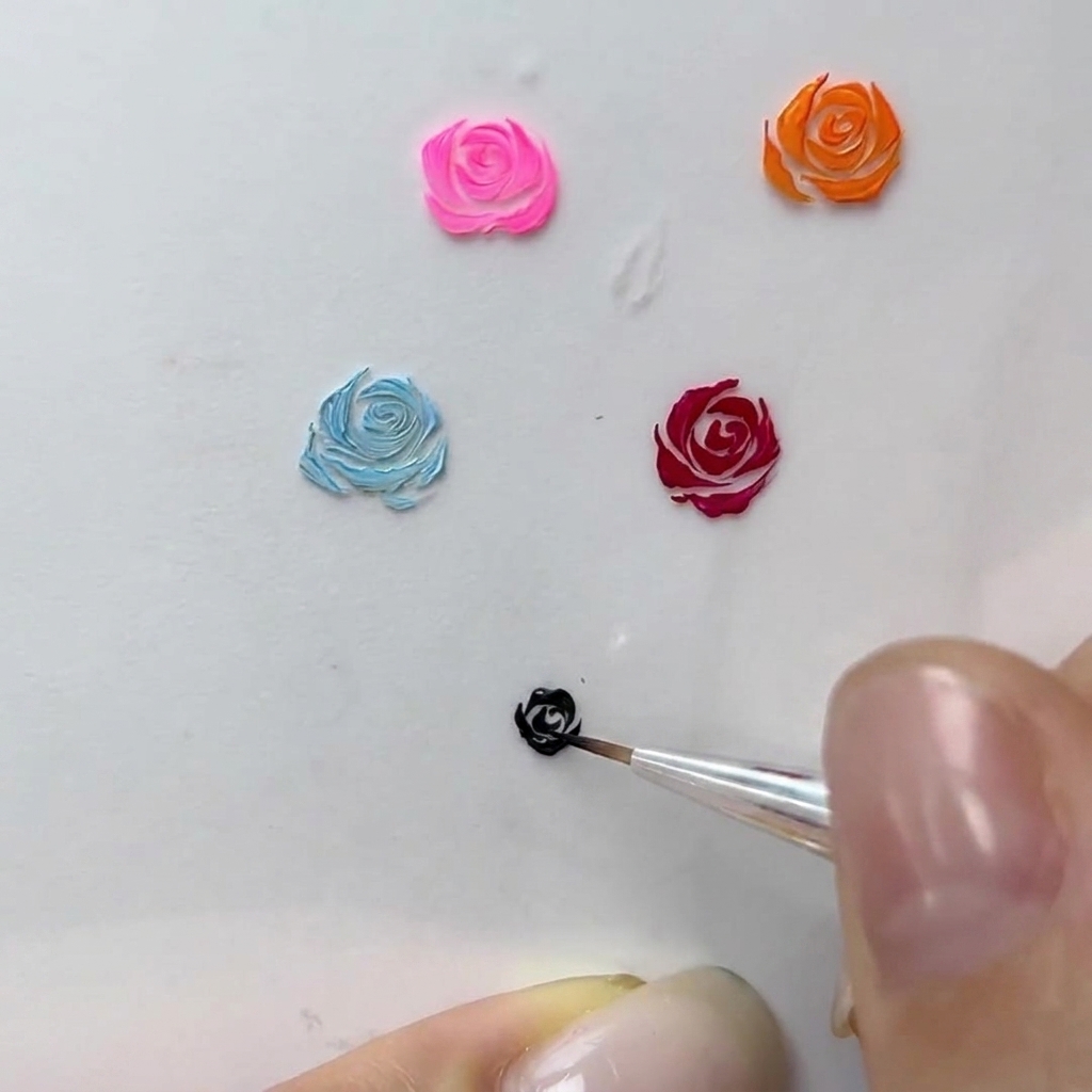 Eine Makroansicht eines Nageldesigners, der feine geschwungene Striche an den Rand einer schwarzen Gelrose anfügt.