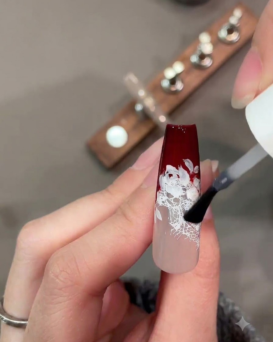 Pędzelek aplikujący matowy top coat na ciemnoczerwono-biały wzór z koronką.