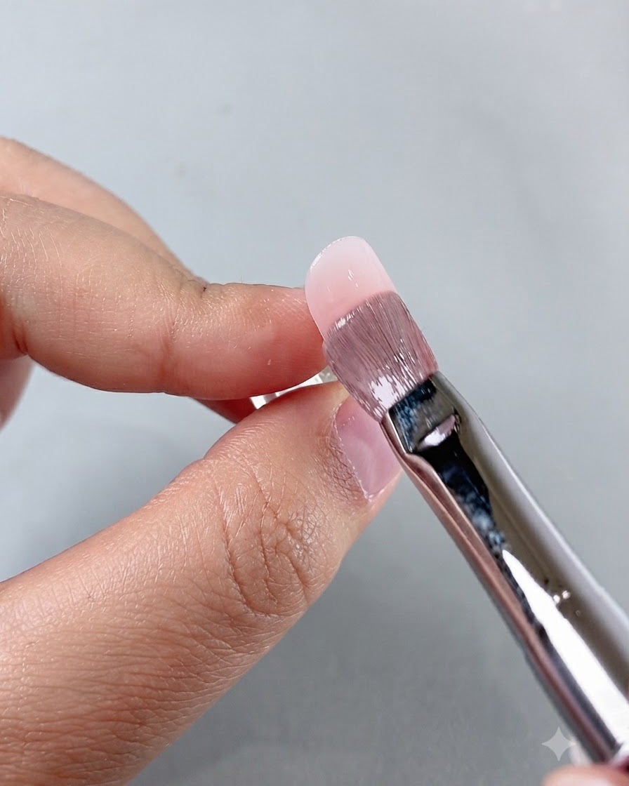 Pędzelek do manicure wygładzający produkt w okolicach skórek podczas pracy nad aplikacją na paznokciu.