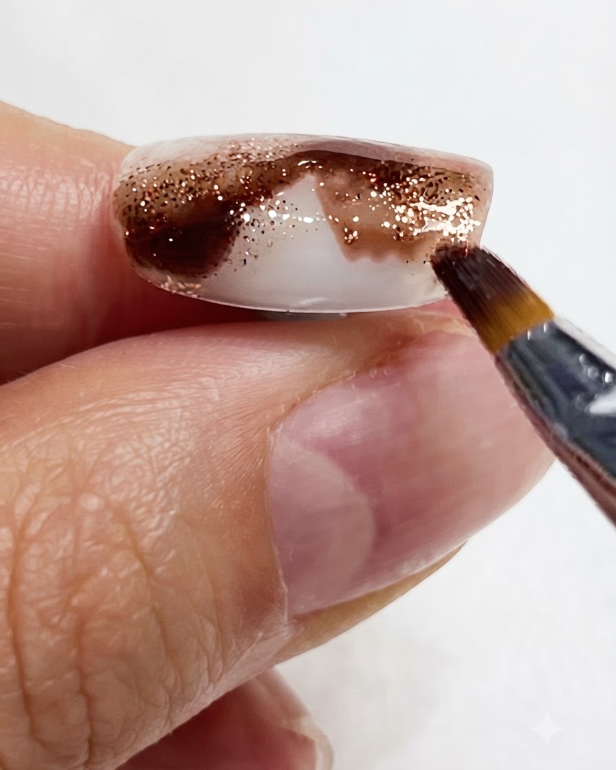 Zbliżenie pokazujące cienki pędzelek przeciągający bursztynowy pigment w dół paznokcia.