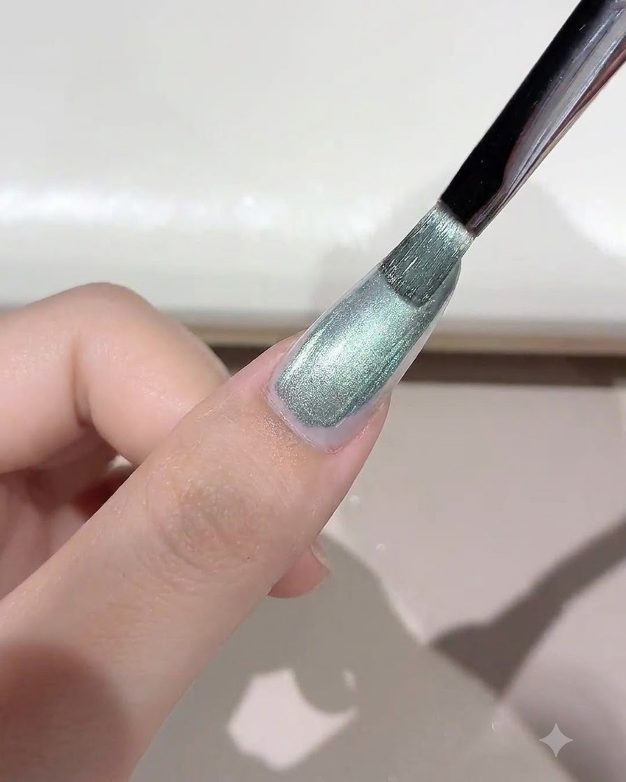 Ein Pinsel trägt ein schimmerndes, grünlich getöntes wildes Cat-Eye-Gel auf den Nagel auf.