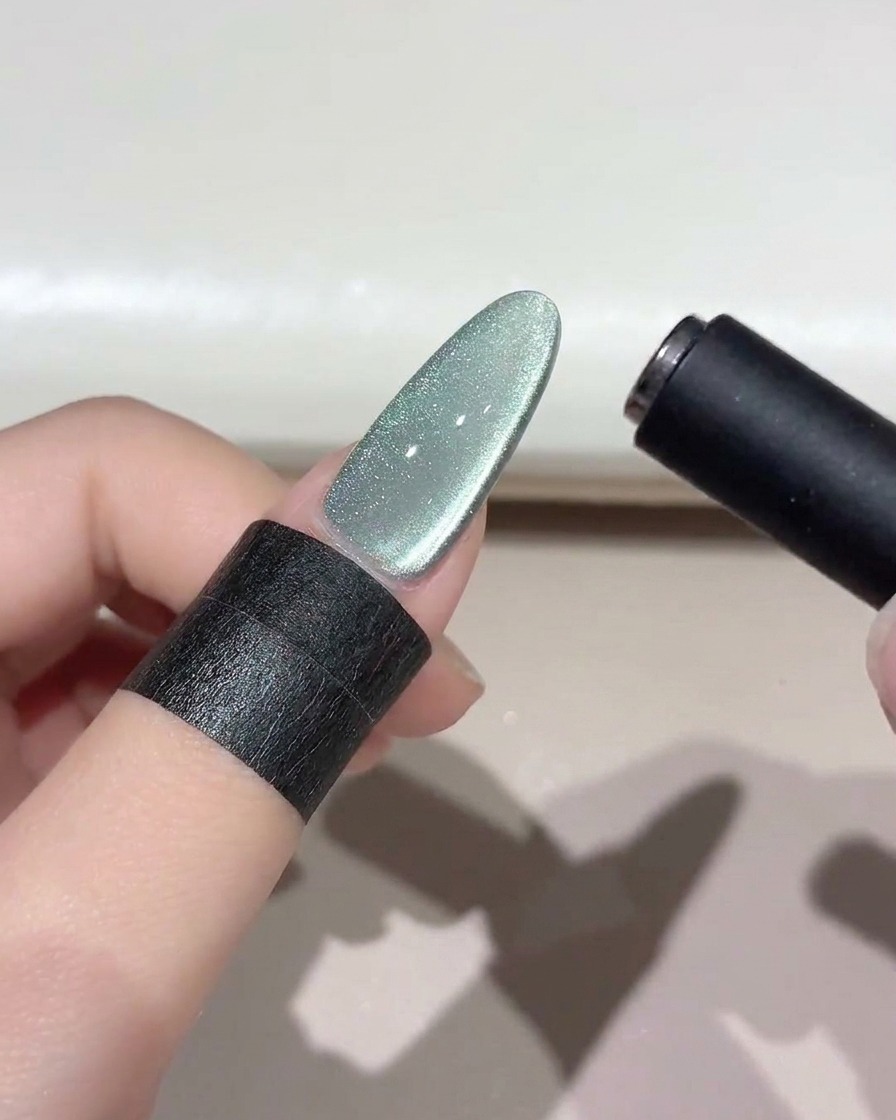 Ein schwarzes Magnetwerkzeug schwebt über einem schimmernden grünen Cat-Eye-Nagel, um das Lichtband zu formen.