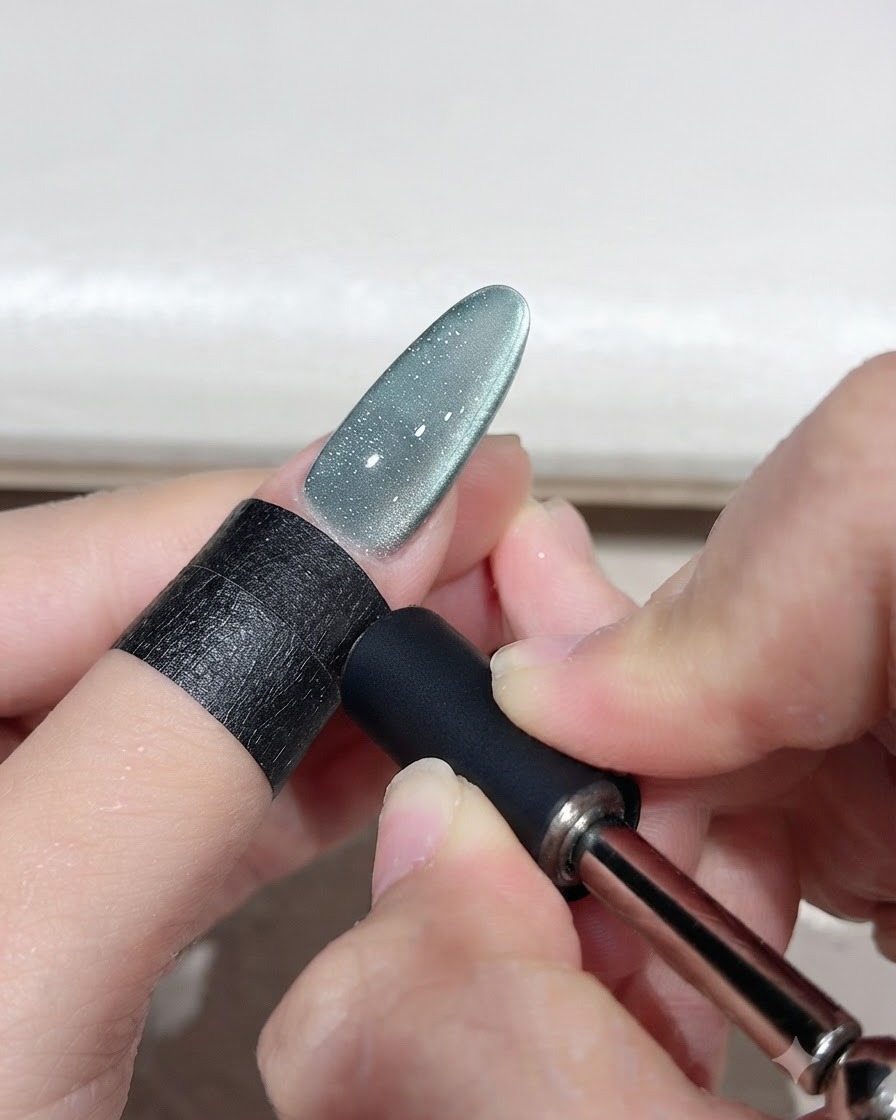 Ein Magnetwerkzeug wird in der Nähe eines grünen Cat-Eye-Gel-Nagels gehalten, um einen geschwungenen Lichtbogen zu formen.