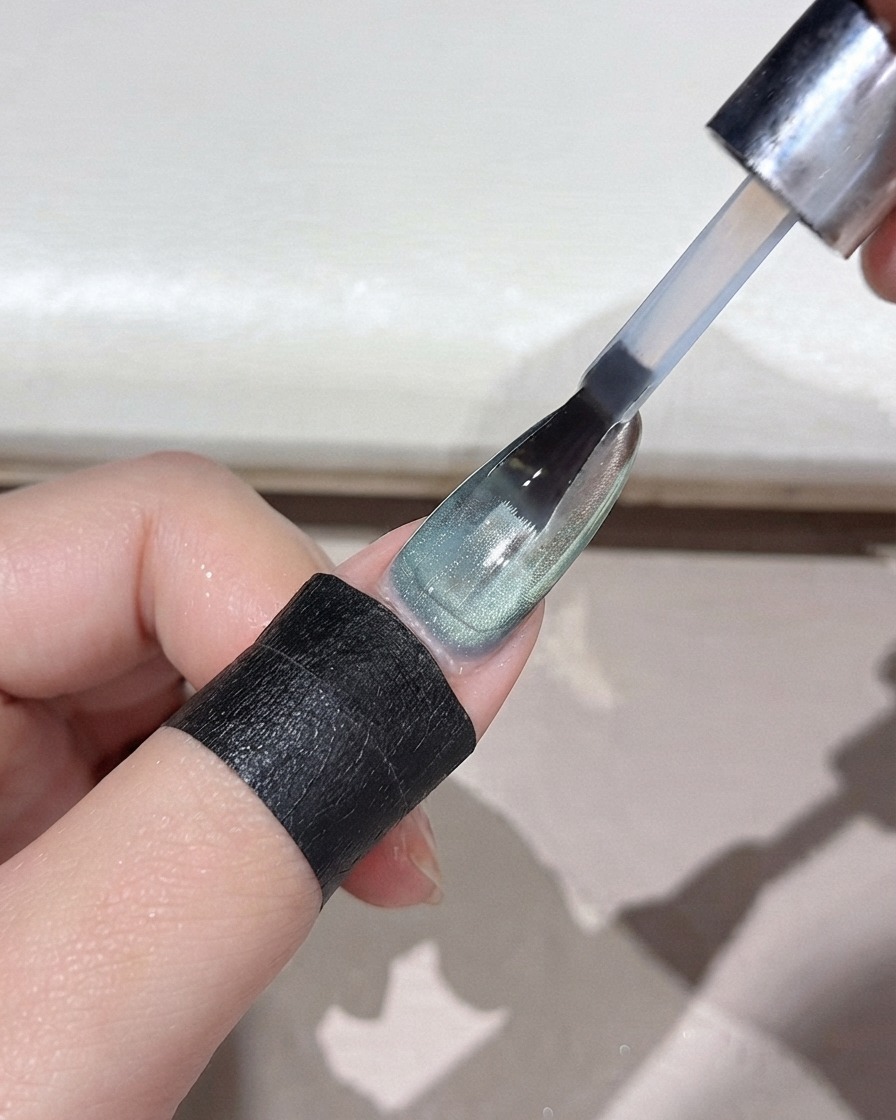 Ein Nagelpinsel trägt einen klaren Topcoat über einem spiegelblanken grünen Puderverlaufsnagel auf.