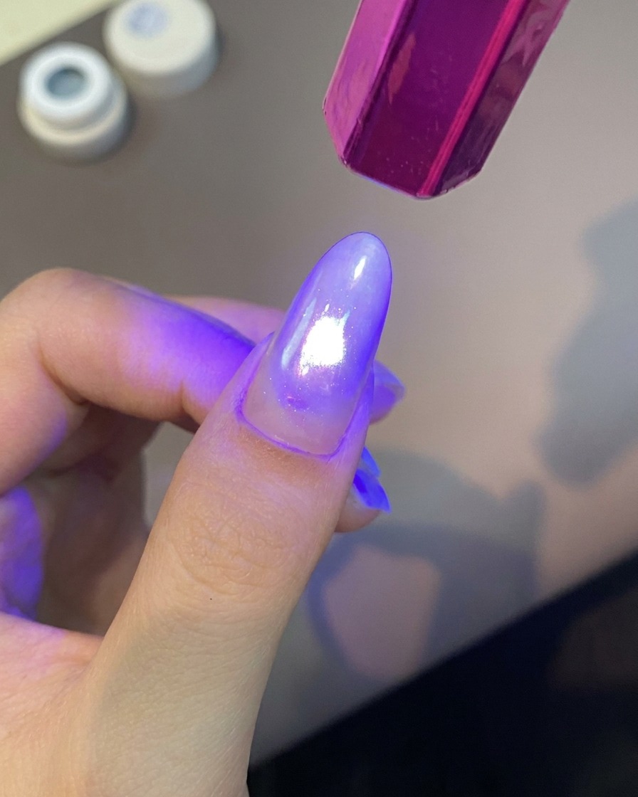 Ręczna fioletowa lampa UV do paznokci świecąca jasnym światłem na pomalowany palec w celu utwardzenia powłoki żelowej.