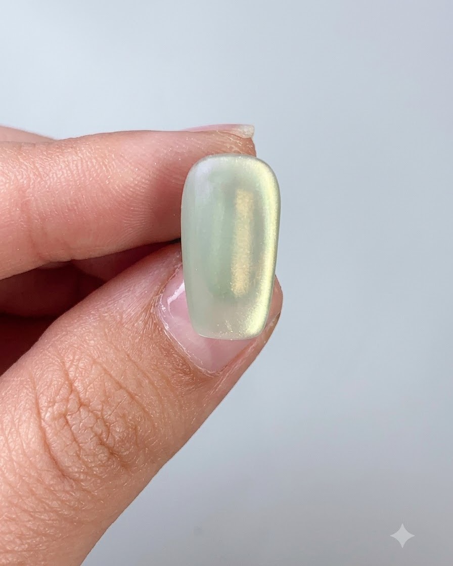 Pędzelek do paznokci nakładający top coat na paznokieć pokryty zielonym żelem cat eye.