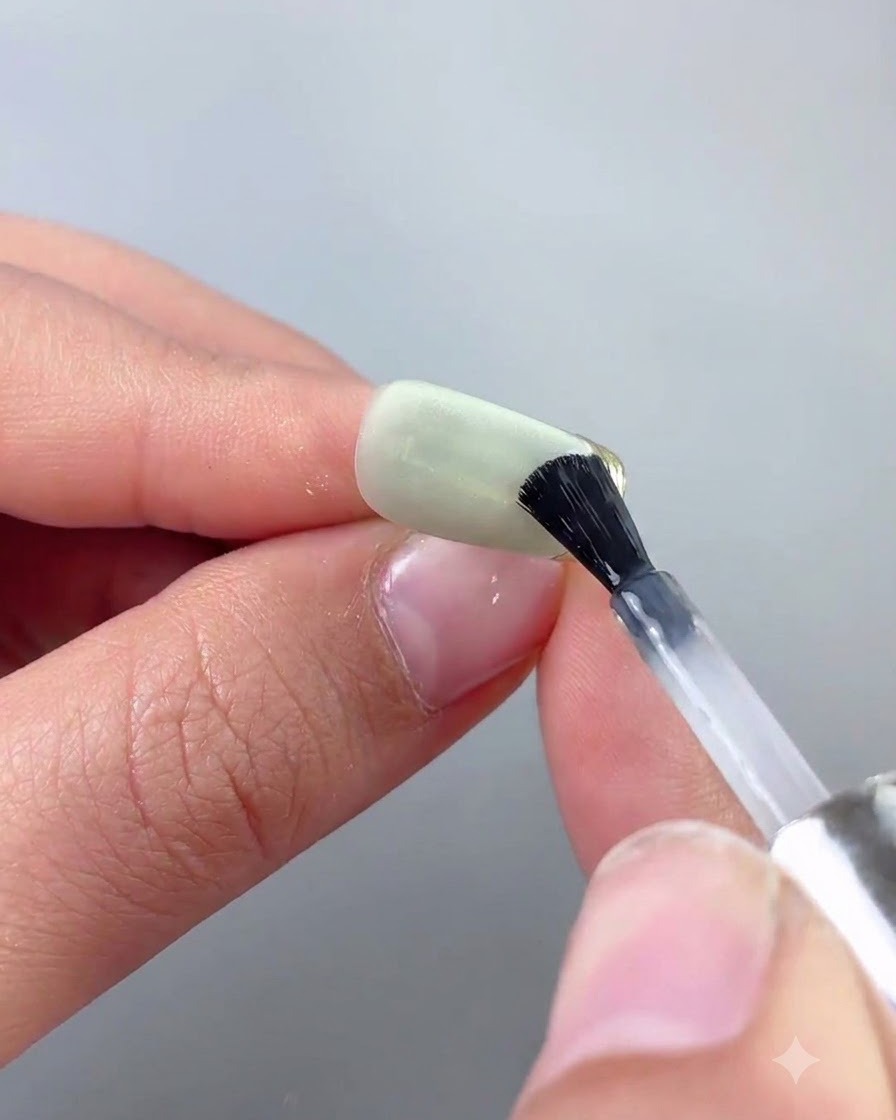 Cienki pędzelek do zdobień paznokci aplikujący top coat precyzyjnie wzdłuż złotej chromowanej krawędzi zielonego paznokcia cat eye.