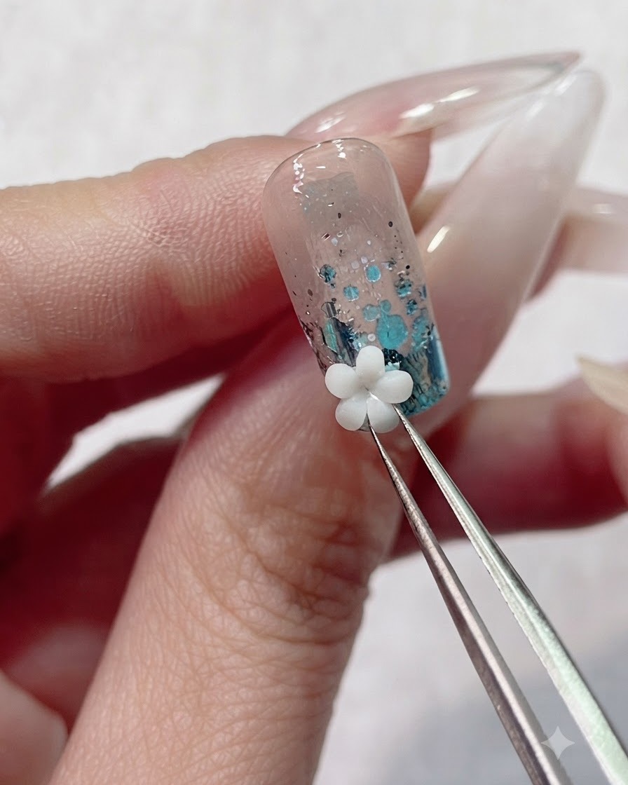 Precyzyjna pęseta umieszczająca białą akrylową ozdobę w kształcie kwiatka 3D na mokrym żelu w pobliżu skórek paznokcia.