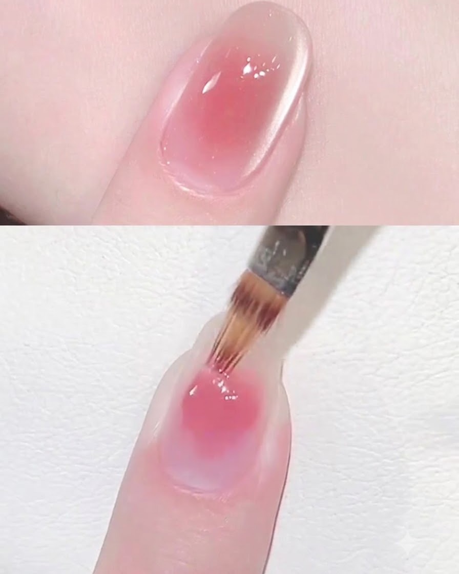 Ein Nagelpinsel trägt eine Schicht klares, schimmerndes Cat Eye Gel über ein rosa Blush-Nageldesign auf.
