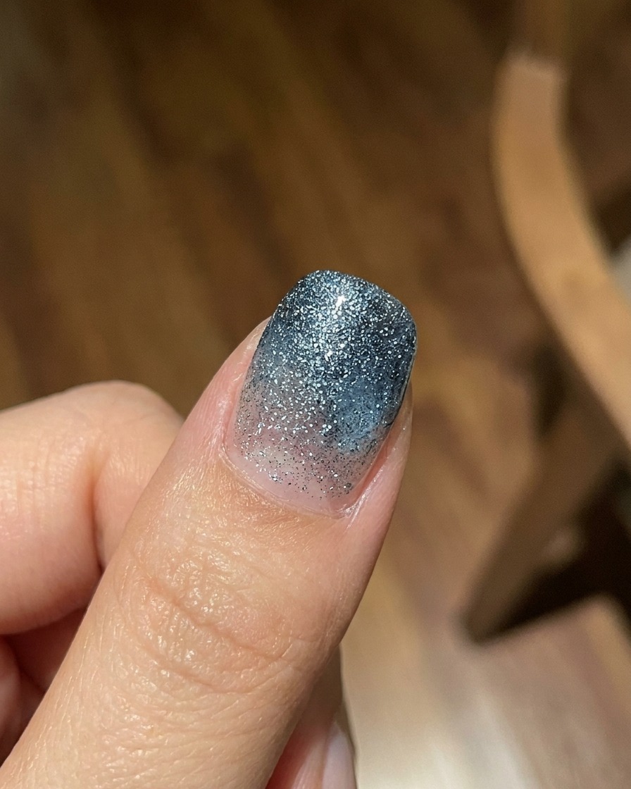 Palec prezentujący półprzezroczystą, niebieską warstwę gradientu żelu jelly na teksturowanym, lśniącym tle, sfotografowany w jasnym świetle naturalnym.