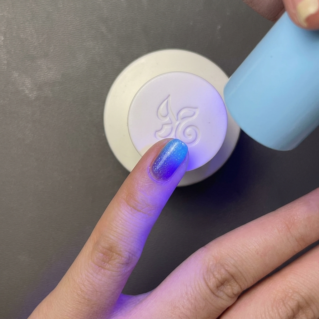 Paletka z jasnoniebieskim lakierem żelowym utwardzana pod małą, przenośną lampą UV/LED o jasnoniebieskim kolorze.