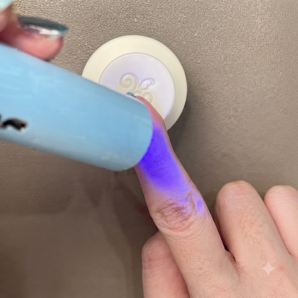 Utwardzanie niebiesko-zielonego paznokcia cat-eye pod małą przenośną niebieską lampą UV/LED.