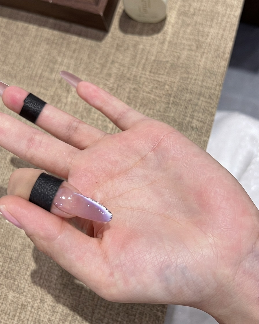Pędzelek aplikujący ostateczny, błyszczący top coat na fioletowy paznokieć ombre cat-eye z cienką srebrną obwódką.