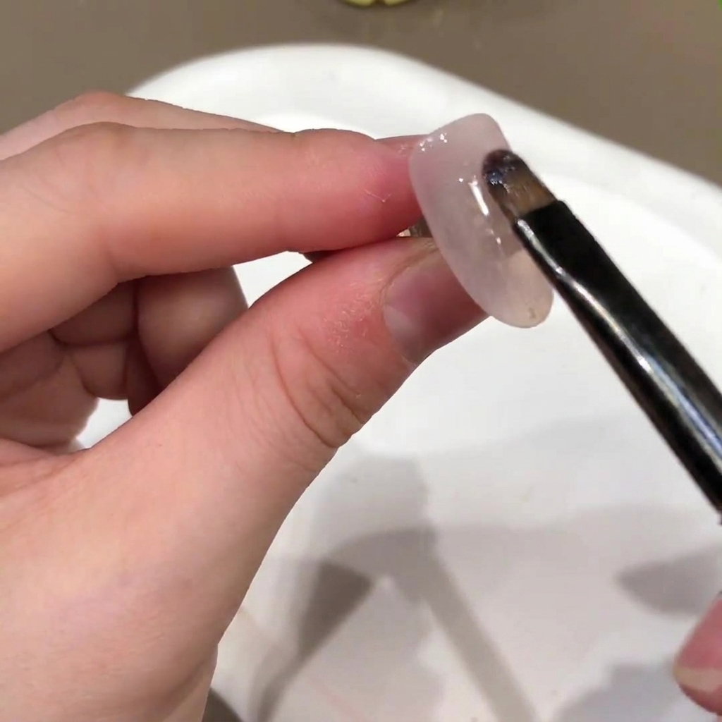 Ein Nagelpinsel trägt eine nudefarbene Gel-Basisfarbe auf die Oberfläche eines künstlichen Nagels auf.