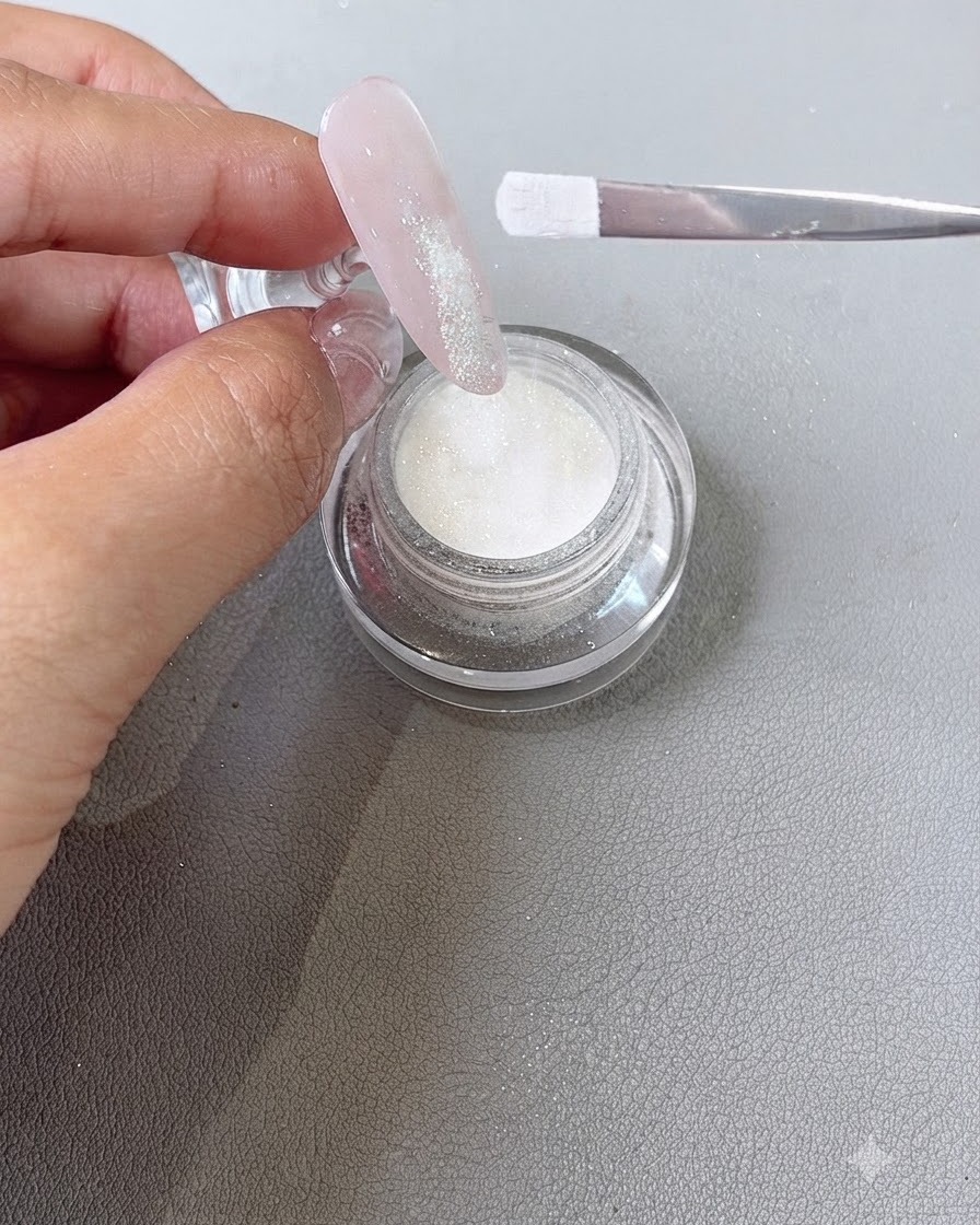Dip-Powder wird mit einem Pinsel auf den feuchten Gel-Spitzenbereich eines Fingers gestreut.