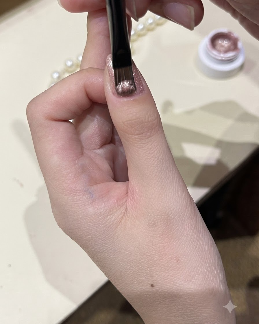 Zbliżenie przedstawiające cienki pędzelek aplikujący mieniący się żel cat-eye na płytkę paznokcia kciuka.