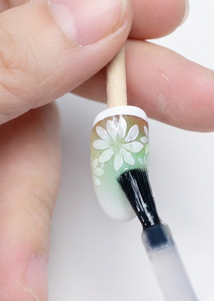 Pędzelek nakładający matowy top coat na wykonane zdobienie z margaritkami.