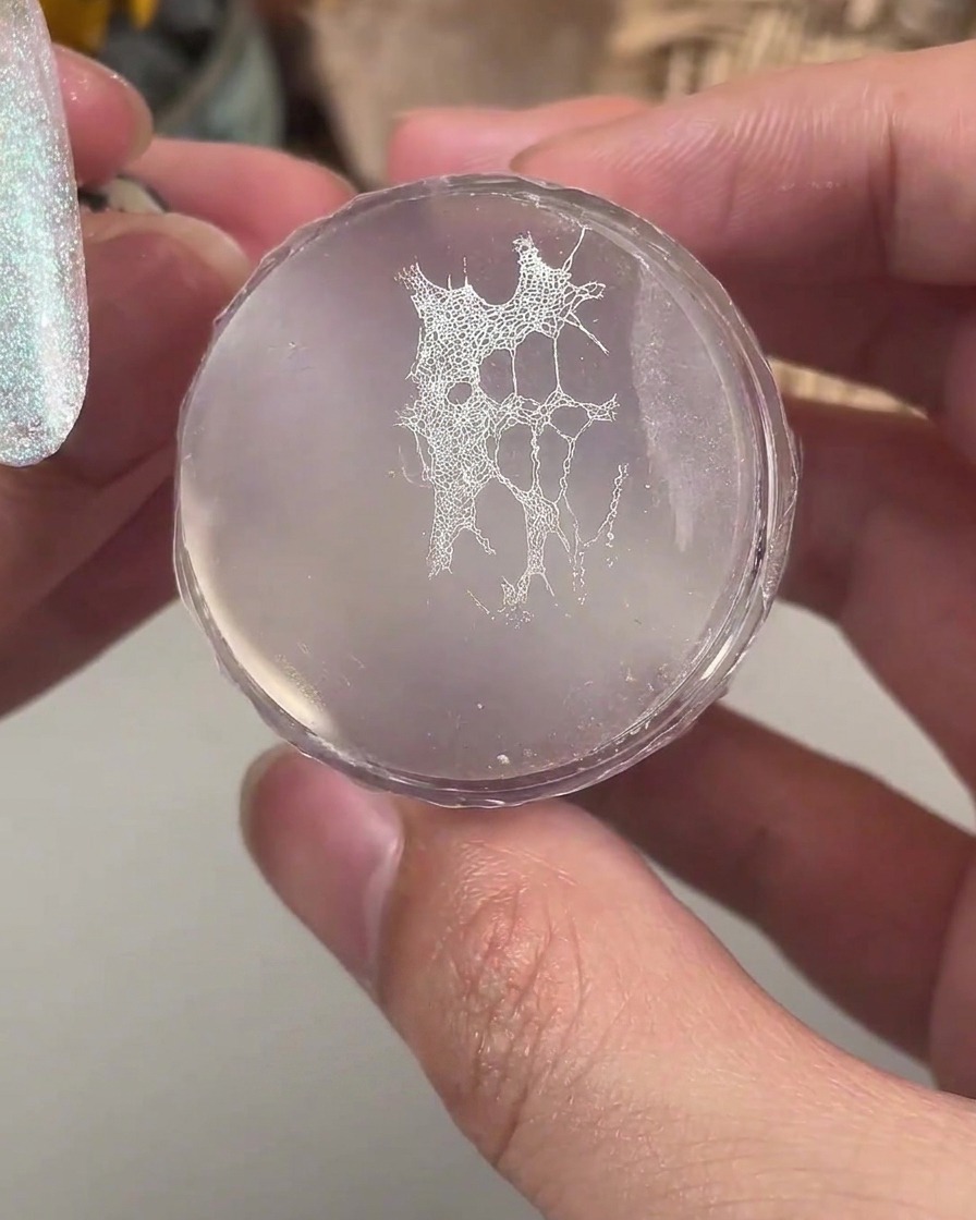 Przezroczysty silikonowy stempel trzymający drobny biały wzór koronki gotowy do przeniesienia na paznokieć.