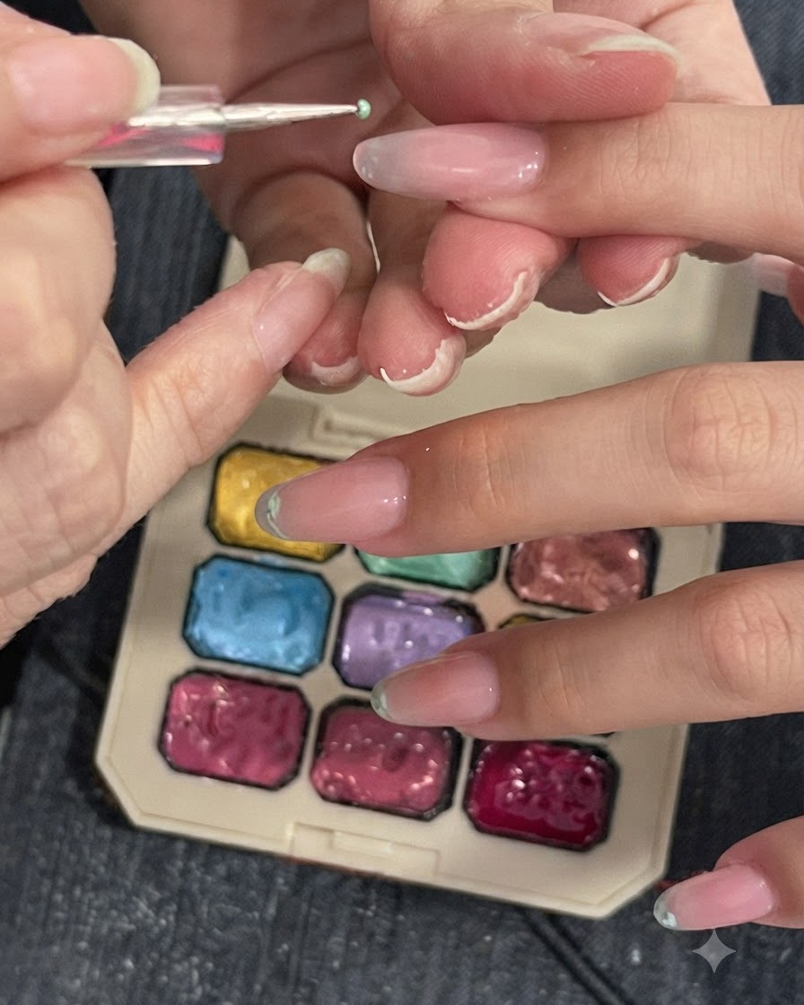 Narzędzie precyzyjne lub gąbeczka wklepująca jasnozielony pigment na końcówkę paznokcia obok palety kolorów.