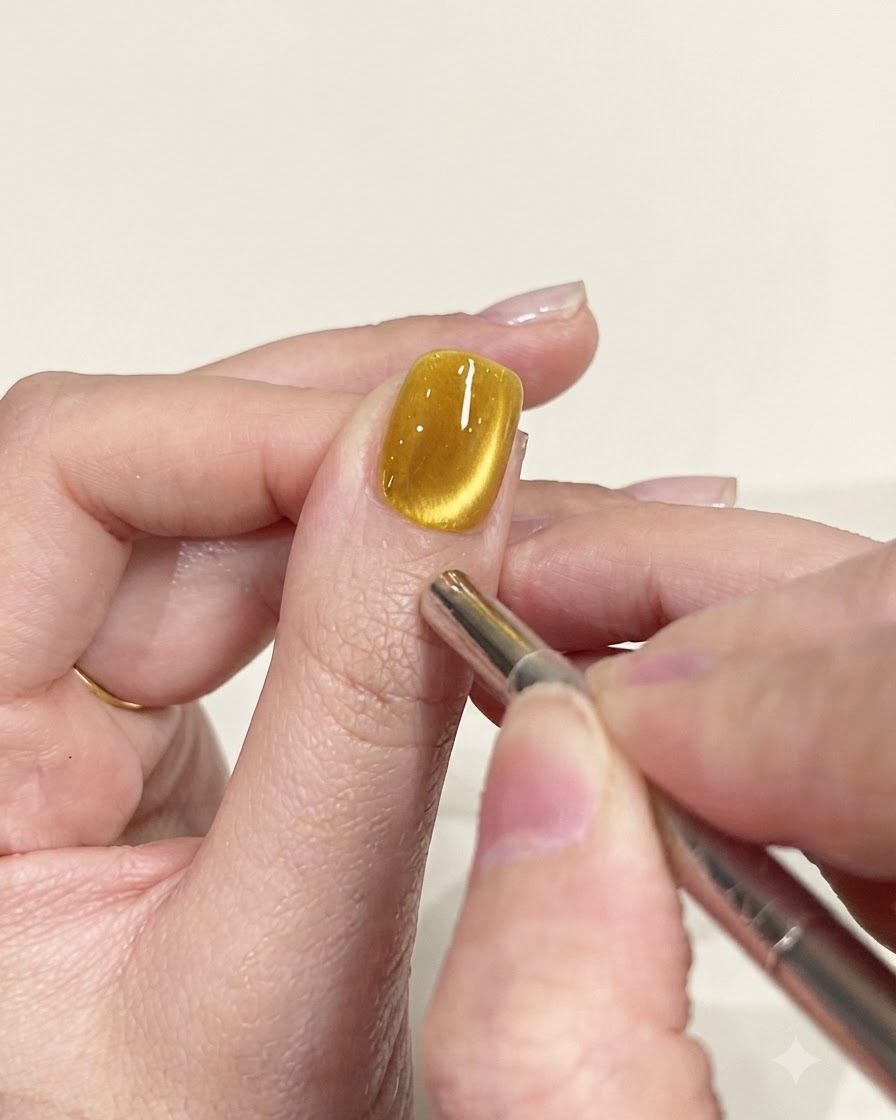 Precyzyjne narzędzie magnetyczne w kształcie długopisu używane do dopracowania ścieżki połysku na żółtym paznokciu cat-eye.