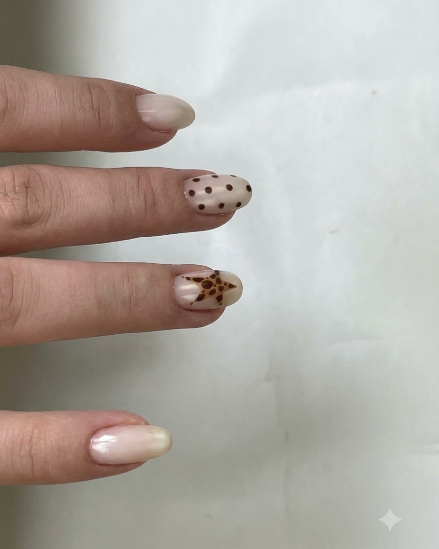 Pędzelek aplikujący klarowny top coat na paznokieć z brązowymi groszkami i motywem gwiazdy.