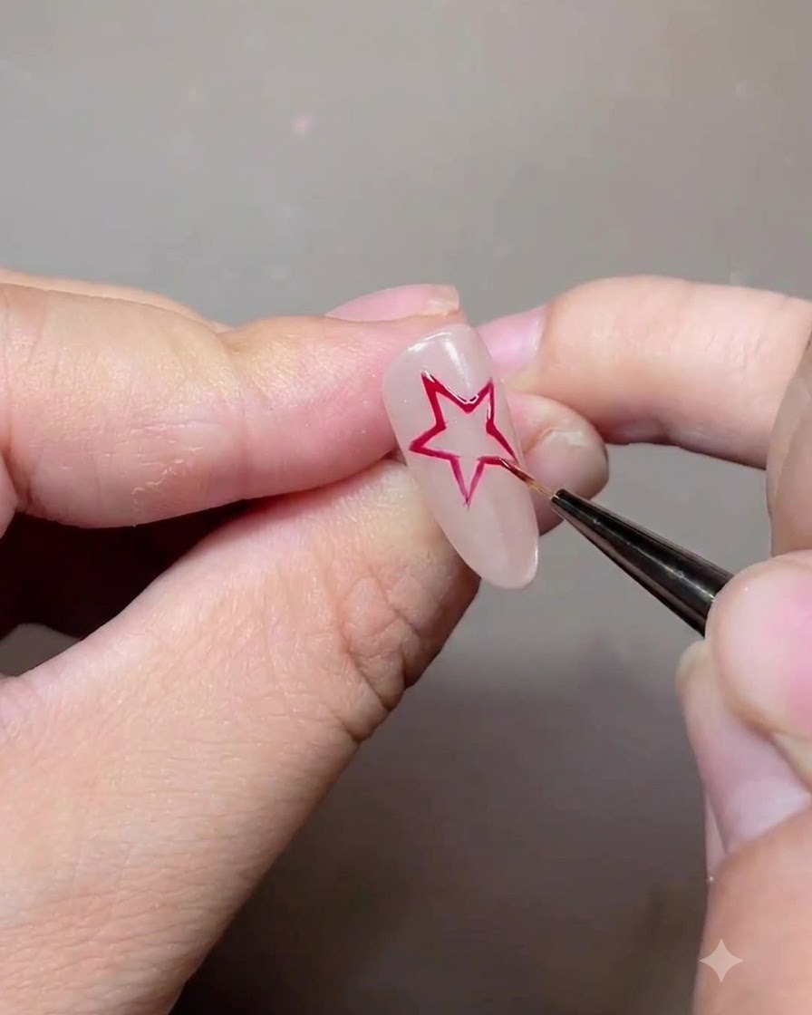 Ein feiner Liner-Pinsel zeichnet einen roten fünfzackigen Sternumriss auf einen Nude-Gel-Nagel.
