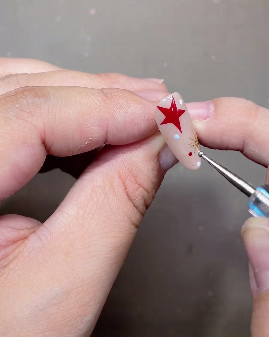 Ein Dotting-Tool platziert winzige weiße und rote Pünktchen auf einem verzierten Nude-Gel-Nagel.