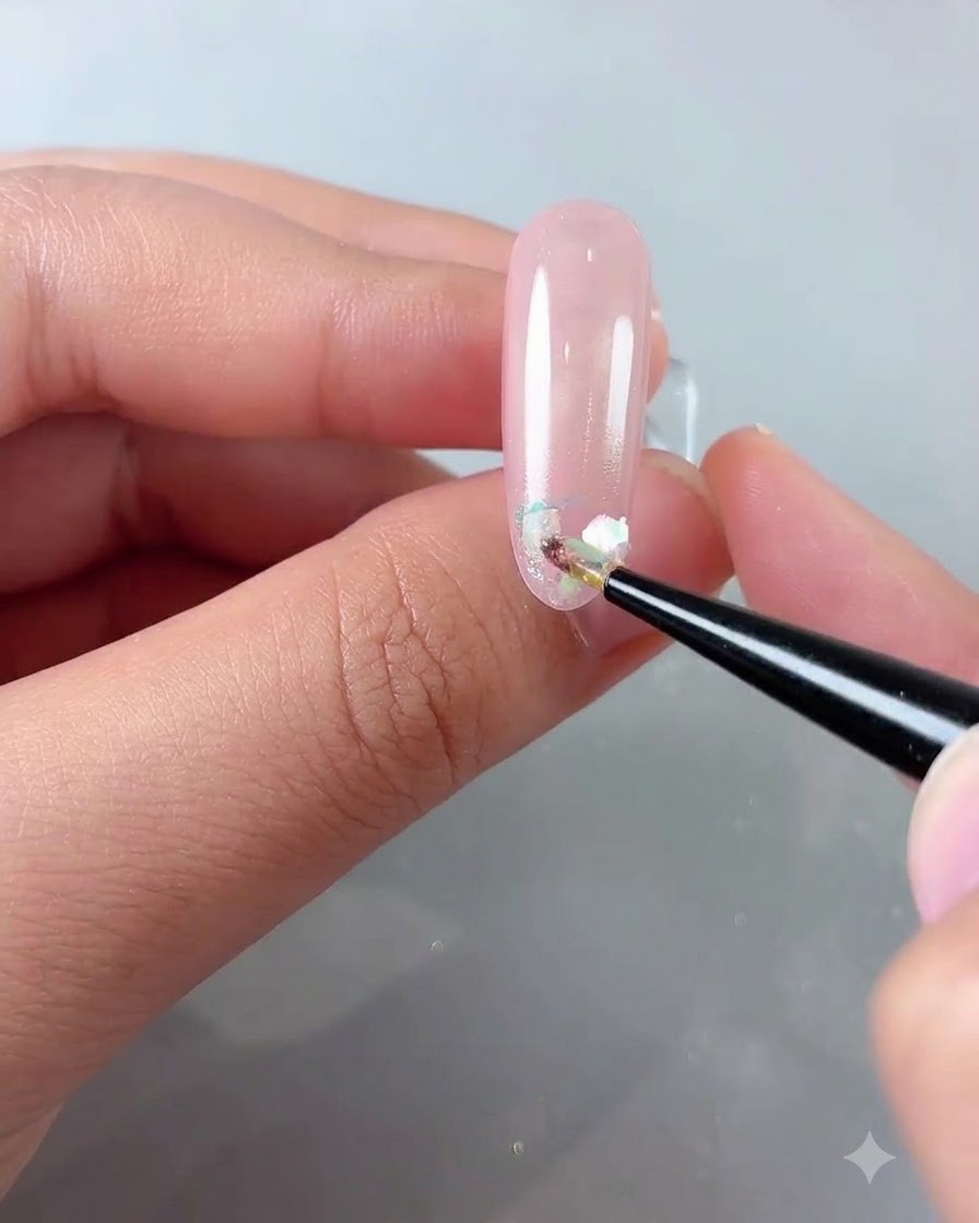 Ein feiner Pinsel platziert irisierende Cloud-Powder-Flocken auf der Vorderkante eines glänzenden rosa Nagels.