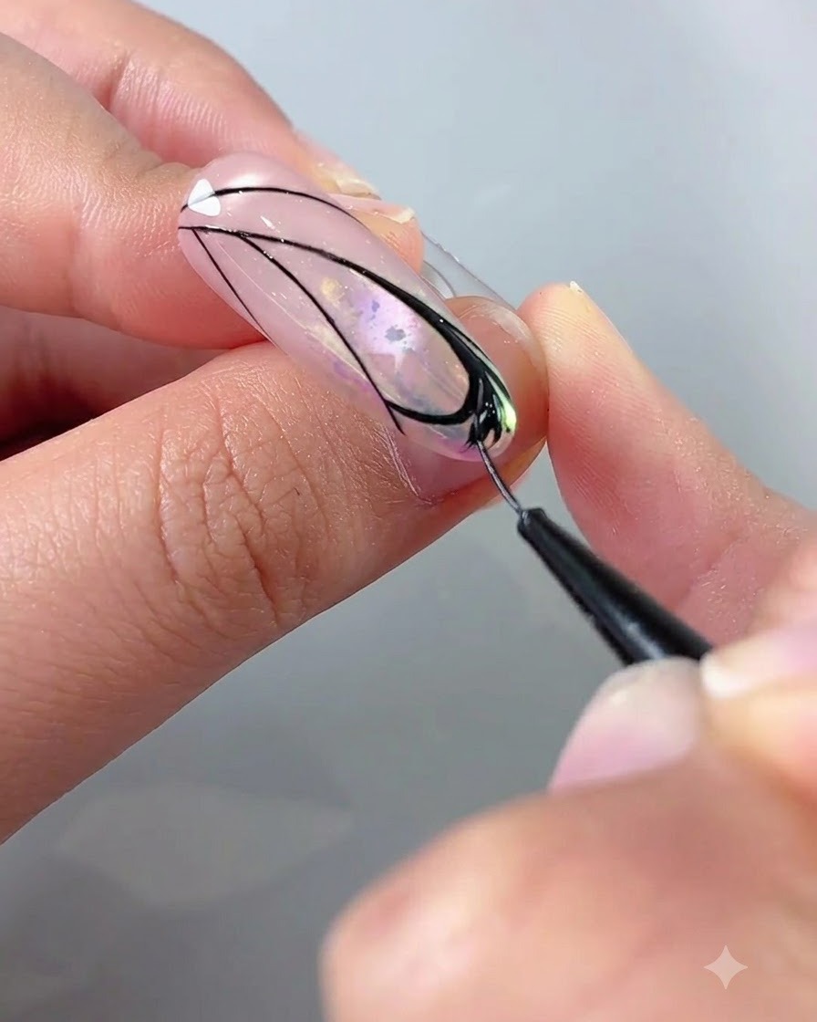 Eine Nahaufnahme einer Hand, die einen Linienpinsel mit schwarzem Gel verwendet, um Details im Schmetterlingsflügeldesign auszufüllen.
