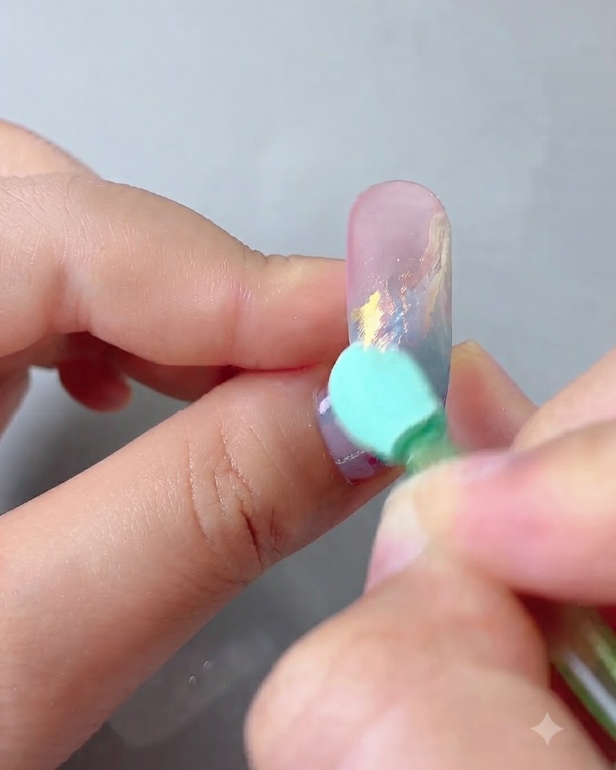 Gąbka aplikacyjna wcierająca pyłek aurora magic mirror w ozdobioną powierzchnię paznokcia.