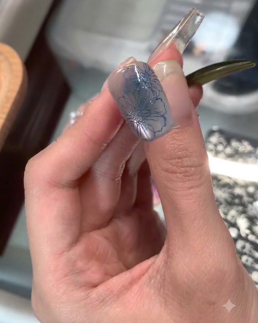 Przezroczysty silikonowy stempel aplikujący delikatny niebieski nadruk kwiatowy na końcówkę palca wskazującego.