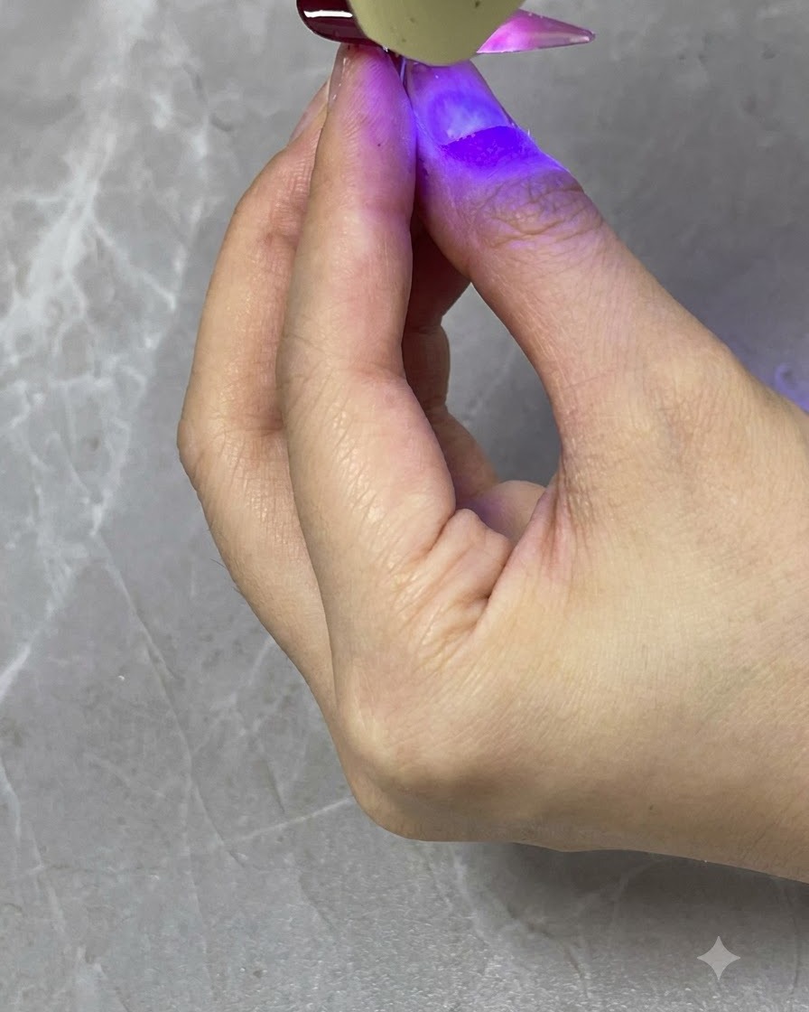 Przenośna lampa UV/LED utwardzająca transparentną czerwoną warstwę gradientową na skończonym paznokciu.