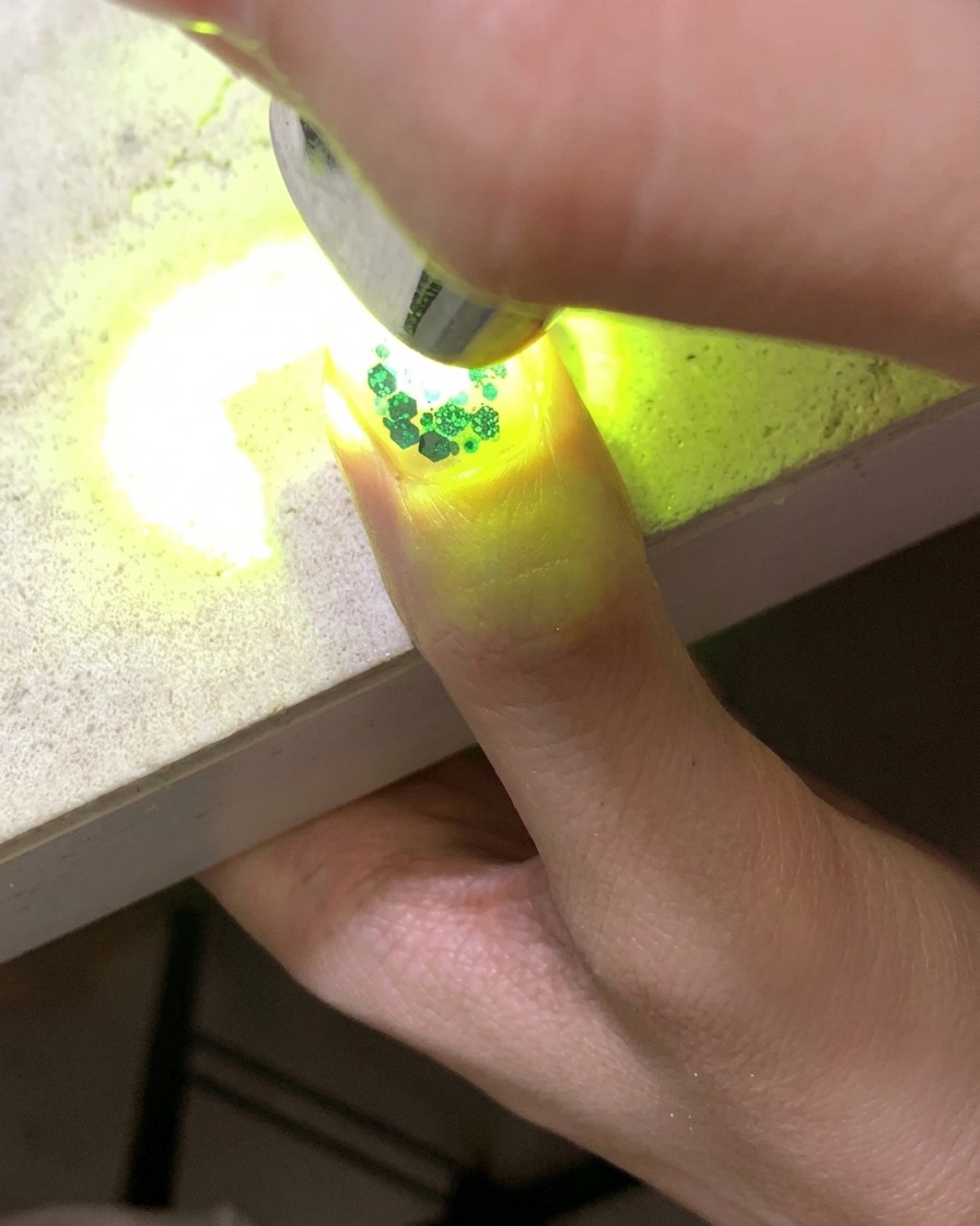 Mini lampa UV utwardzająca paznokieć ozdobiony brokatem i cekinami w kształcie gwiazd.