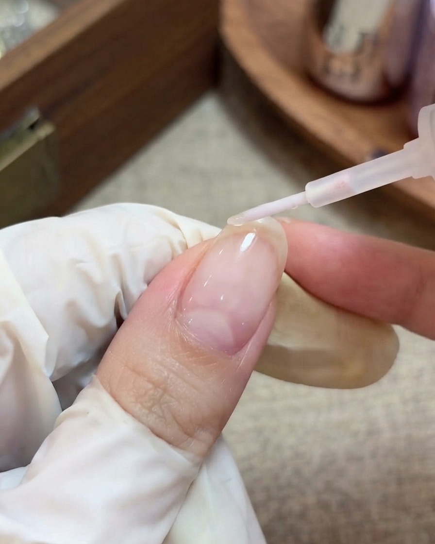 Eine handgeschmückte Hand mit Handschuh verwendet einen Pinsel, um einen klaren, glänzenden Top-Coat über einen vorbereiteten Nagel mit eingekapselten Stern-Glitzern aufzutragen.