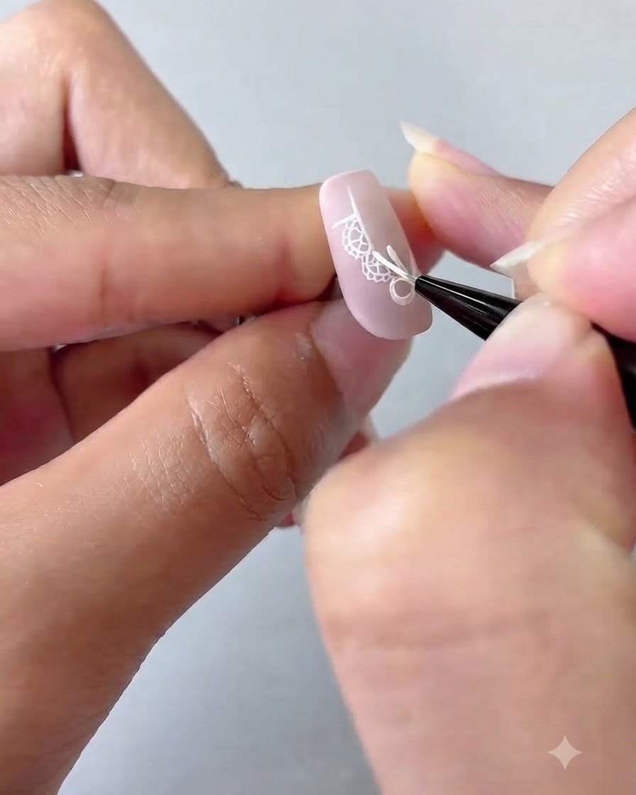 Pędzelek do nail art dodający szczegółowe białe kropki i czteroramienną gwiazdę na paznokciu z różowym gradientem.