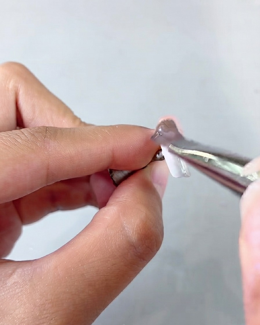 Para pęset trzymająca tips podczas nakładania warstwy żelu cat-eye.