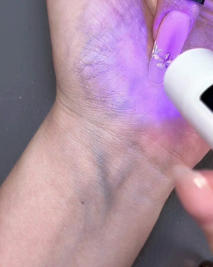 Przenośna mini lampa UV utwardzająca kwiatowy wzór na paznokciu pod fioletowym światłem.